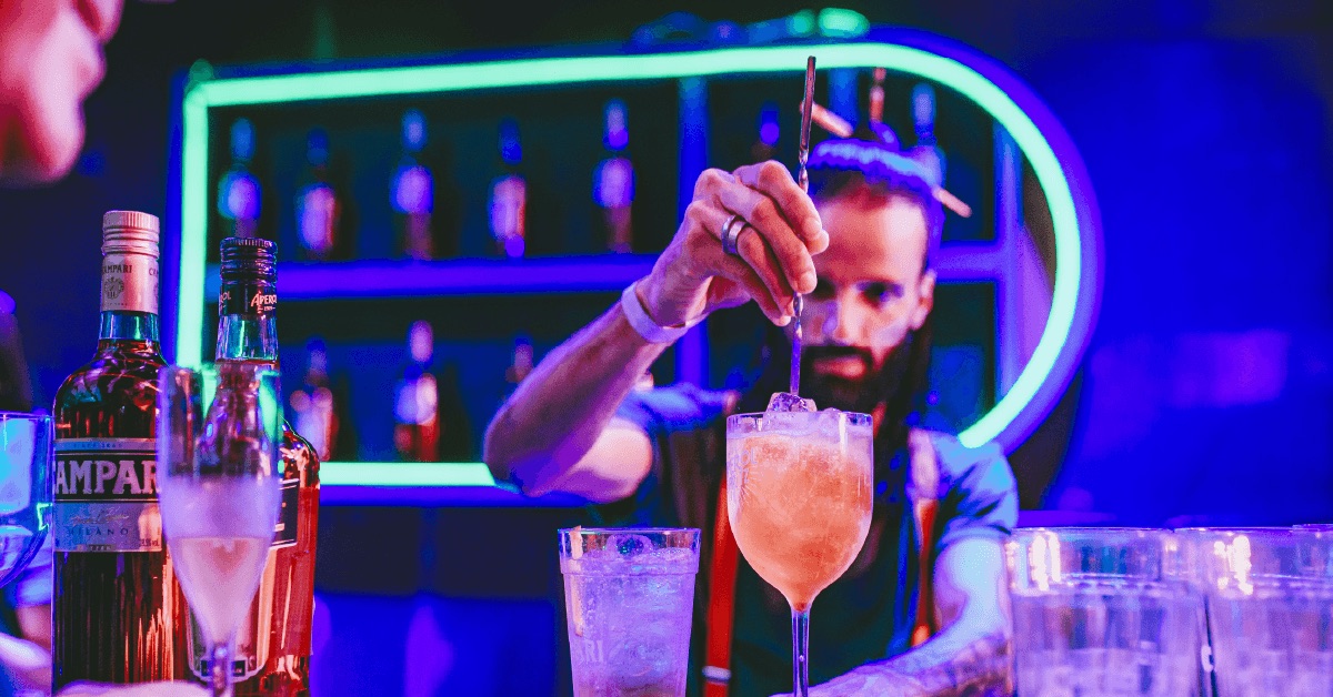 Bartender mixing a cocktail at the Camarote open bar under neon lights